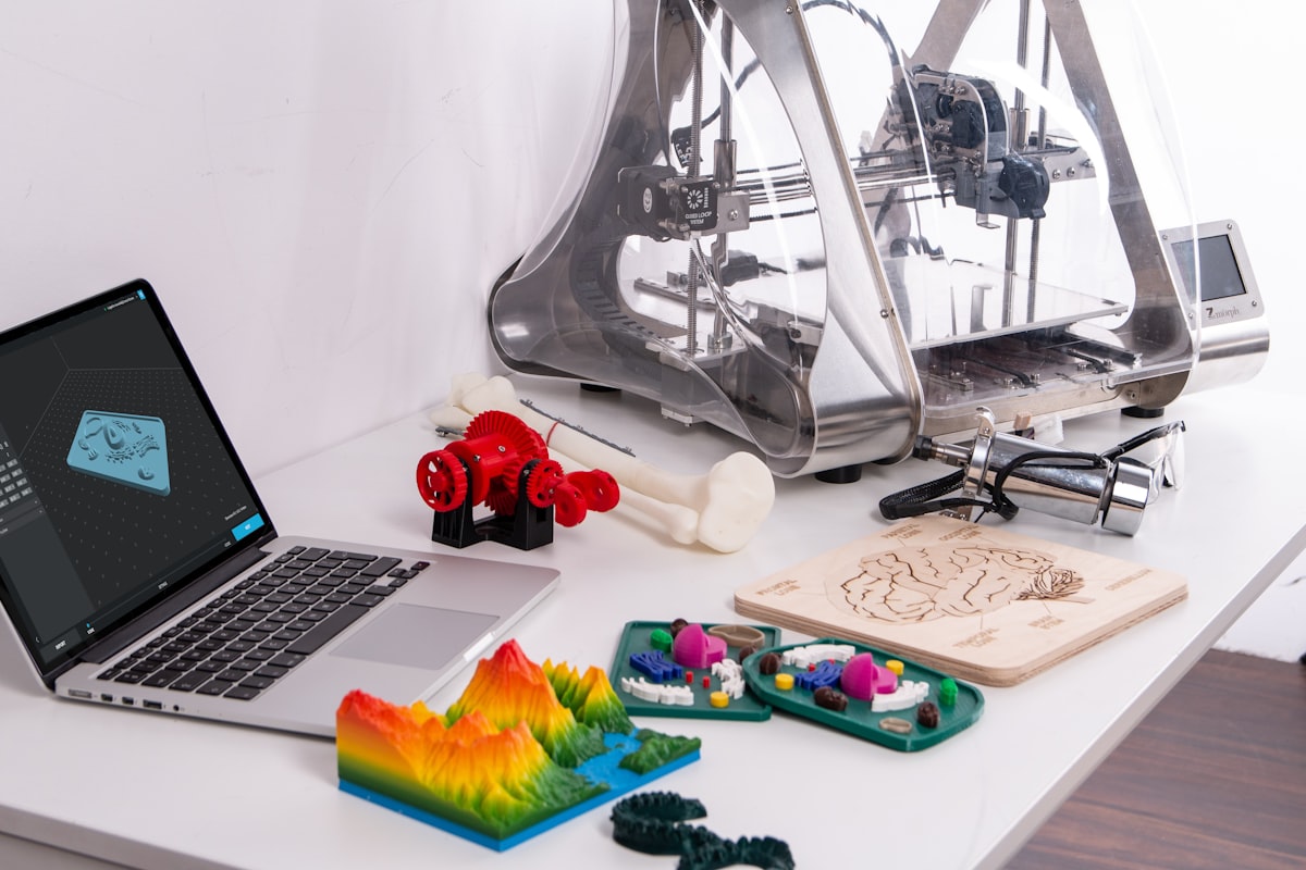 3D printer with colourful printed models and design software on a laptop